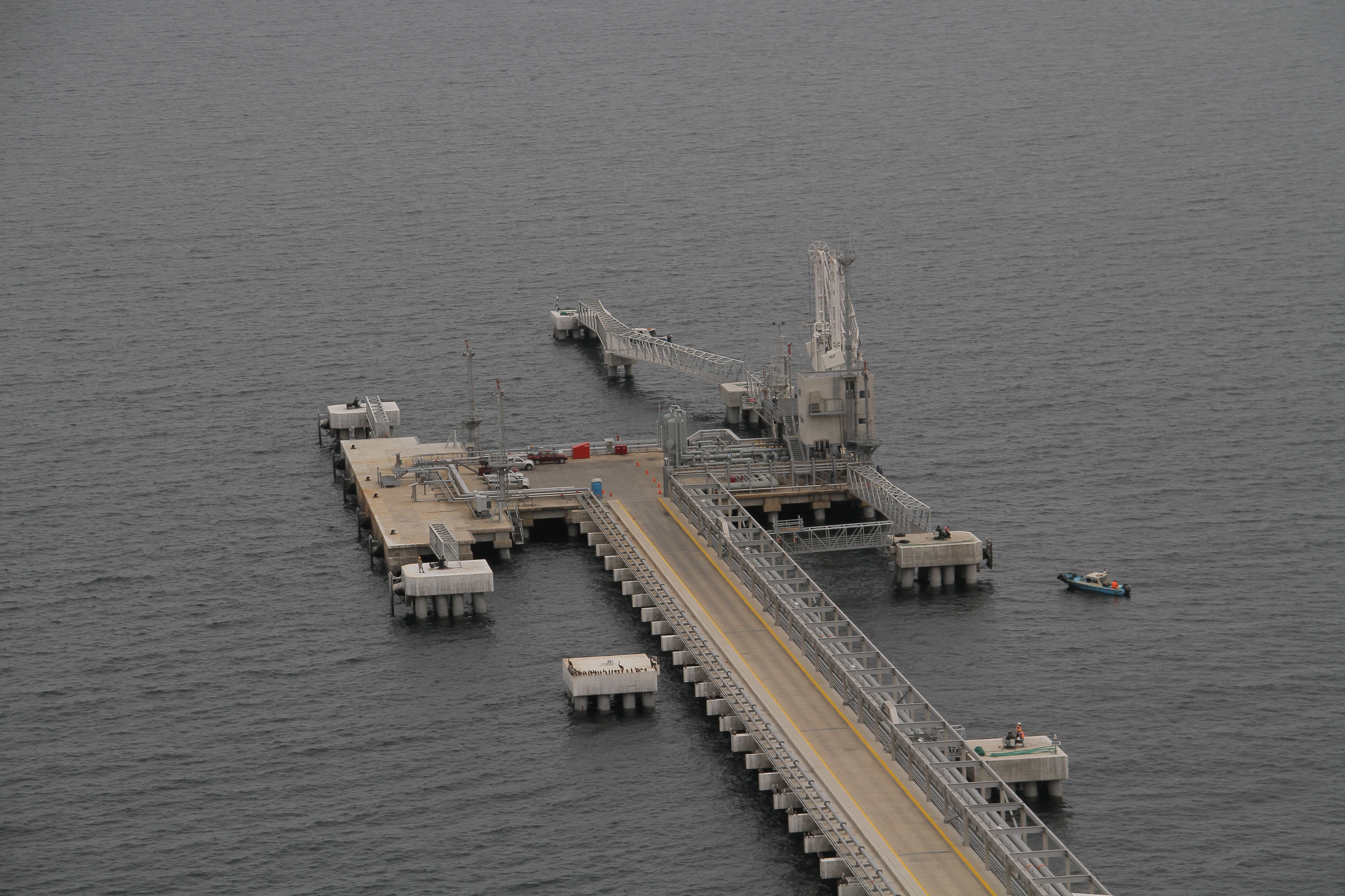KJ Reports, Middle East — An expansive aerial view of the Kharg Island oil terminal infrastructure jutting into the deep blue waters of the Persian Gulf, wit…
