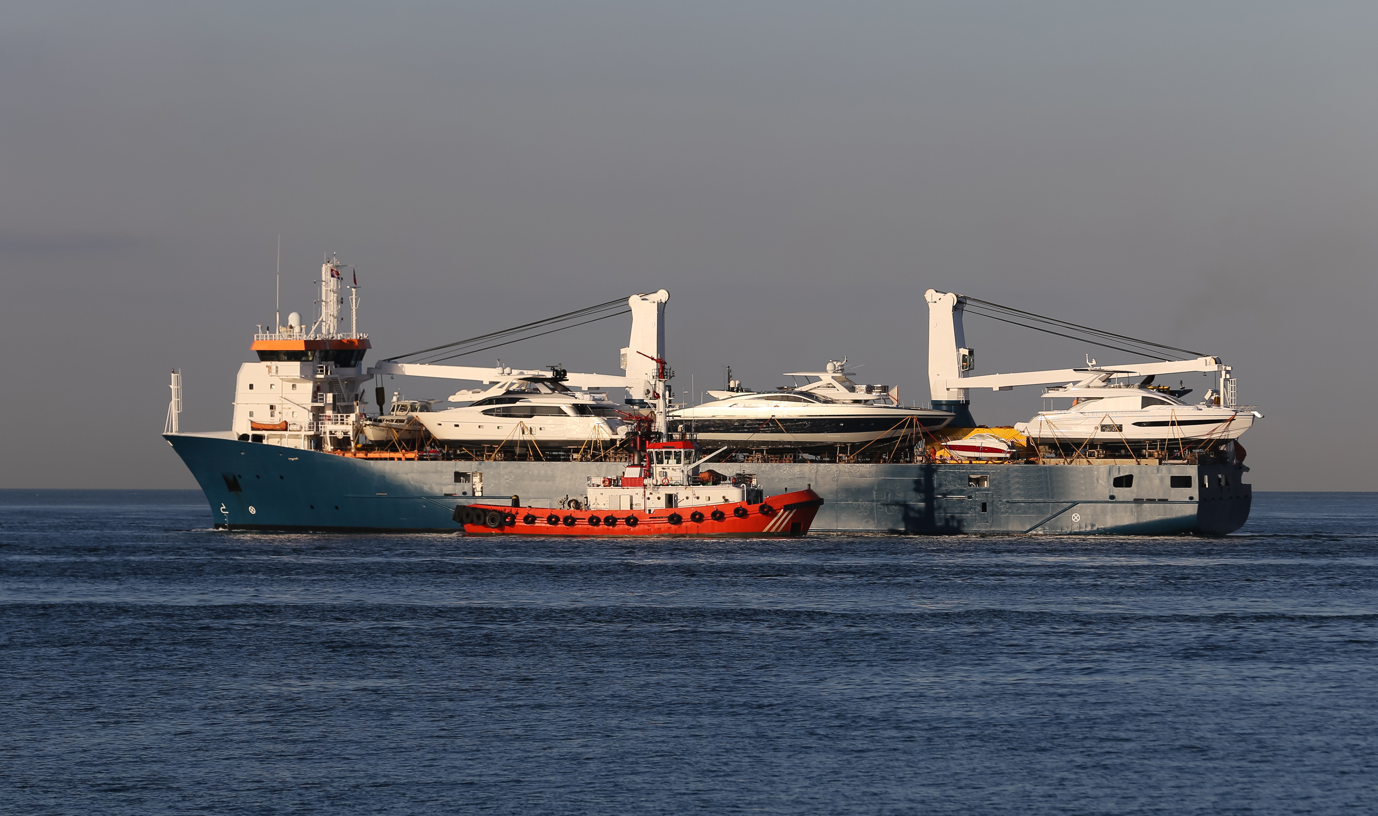KJ Reports, Global — A wide-angle view of a massive container ship passing through the narrow, tropical waters of the Sunda Strait with the Indonesian coastl…