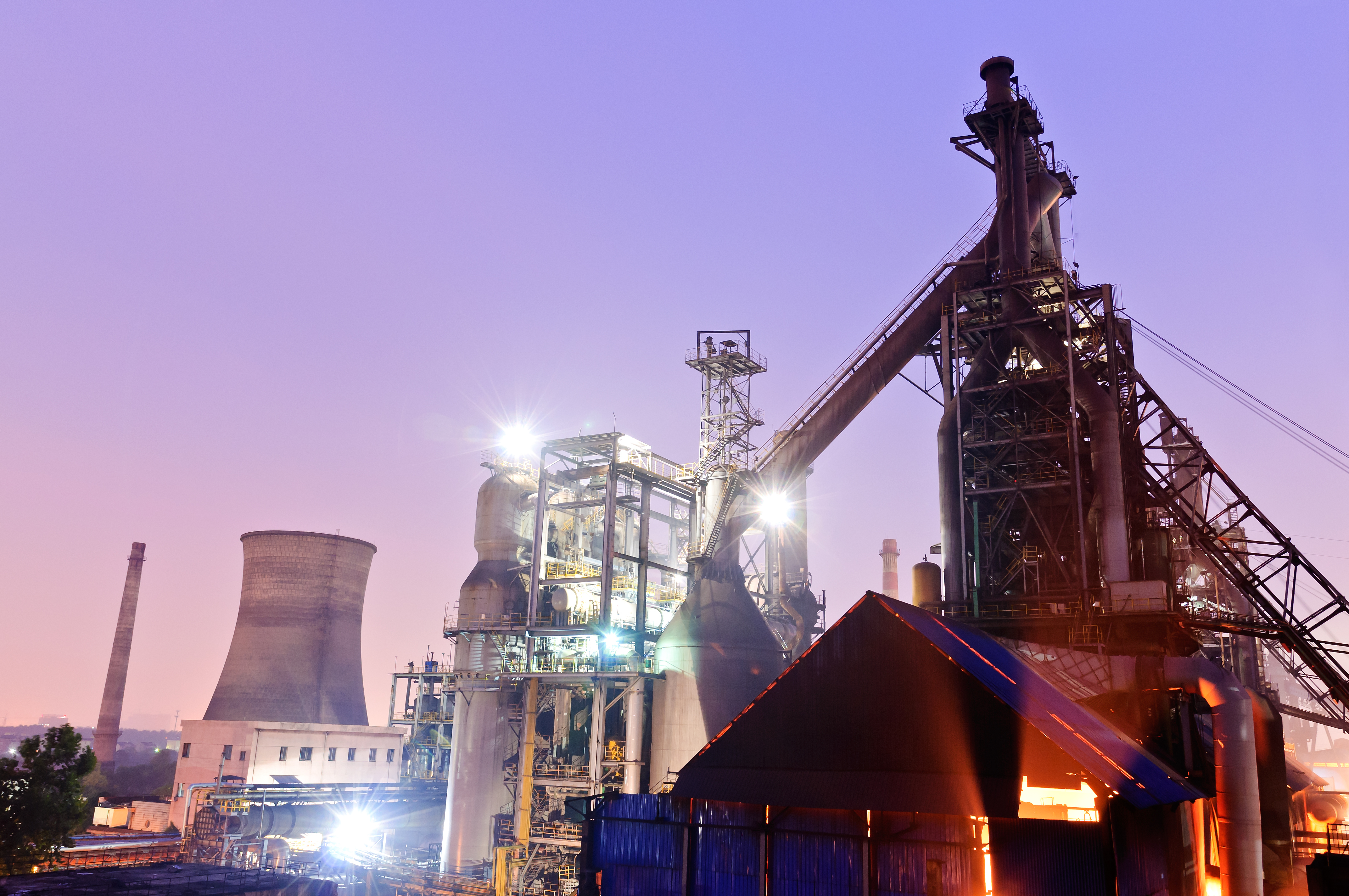 KJ Reports, Global — A sprawling, dimly lit industrial landscape of the Ruhr Valley at dusk, with cooling towers and smokestacks silhouetted against a cold g…