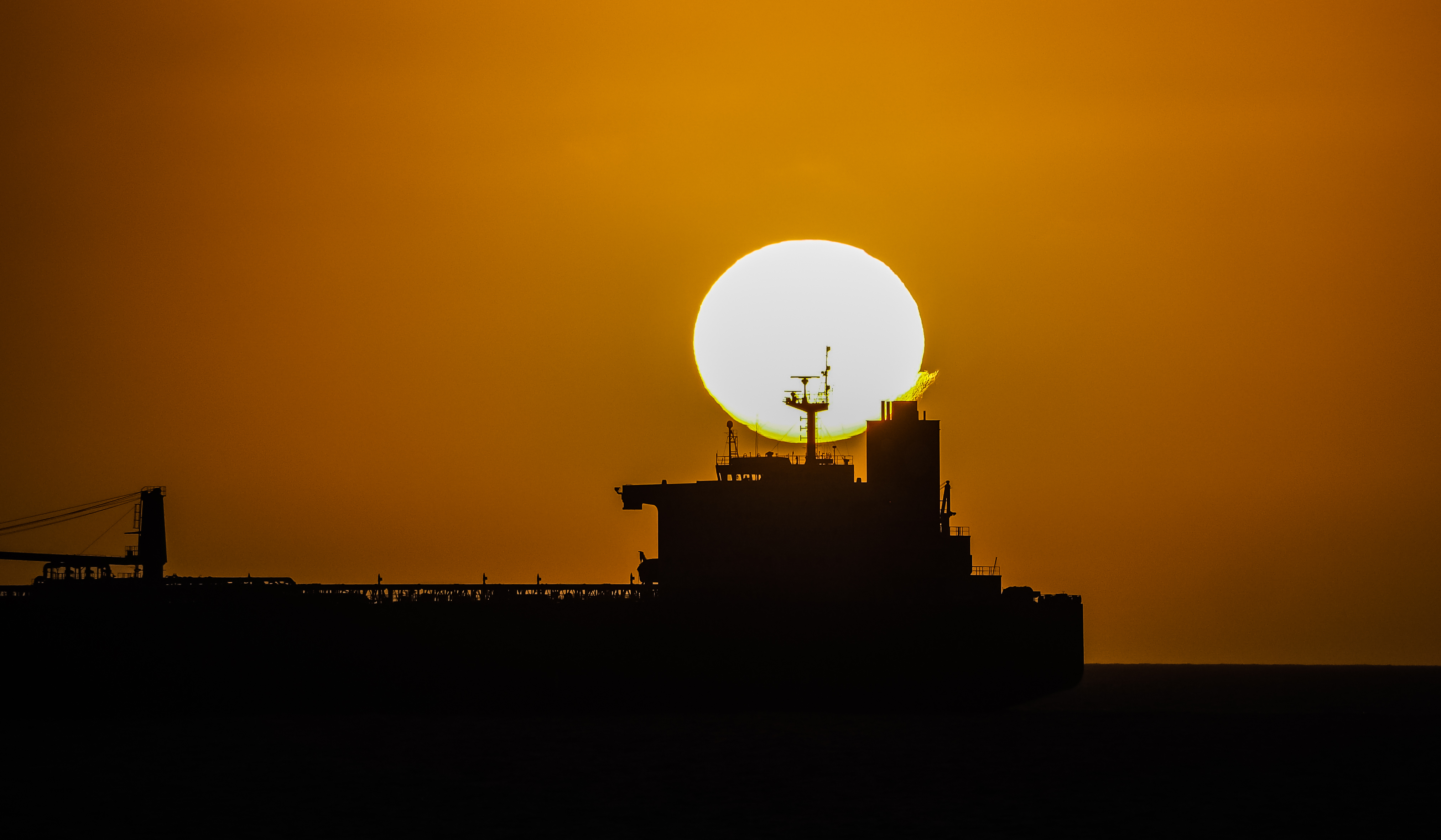KJ Reports, Middle East — A satellite-style perspective showing the narrow Strait of Hormuz with silhouettes of several large oil tankers positioned between…
