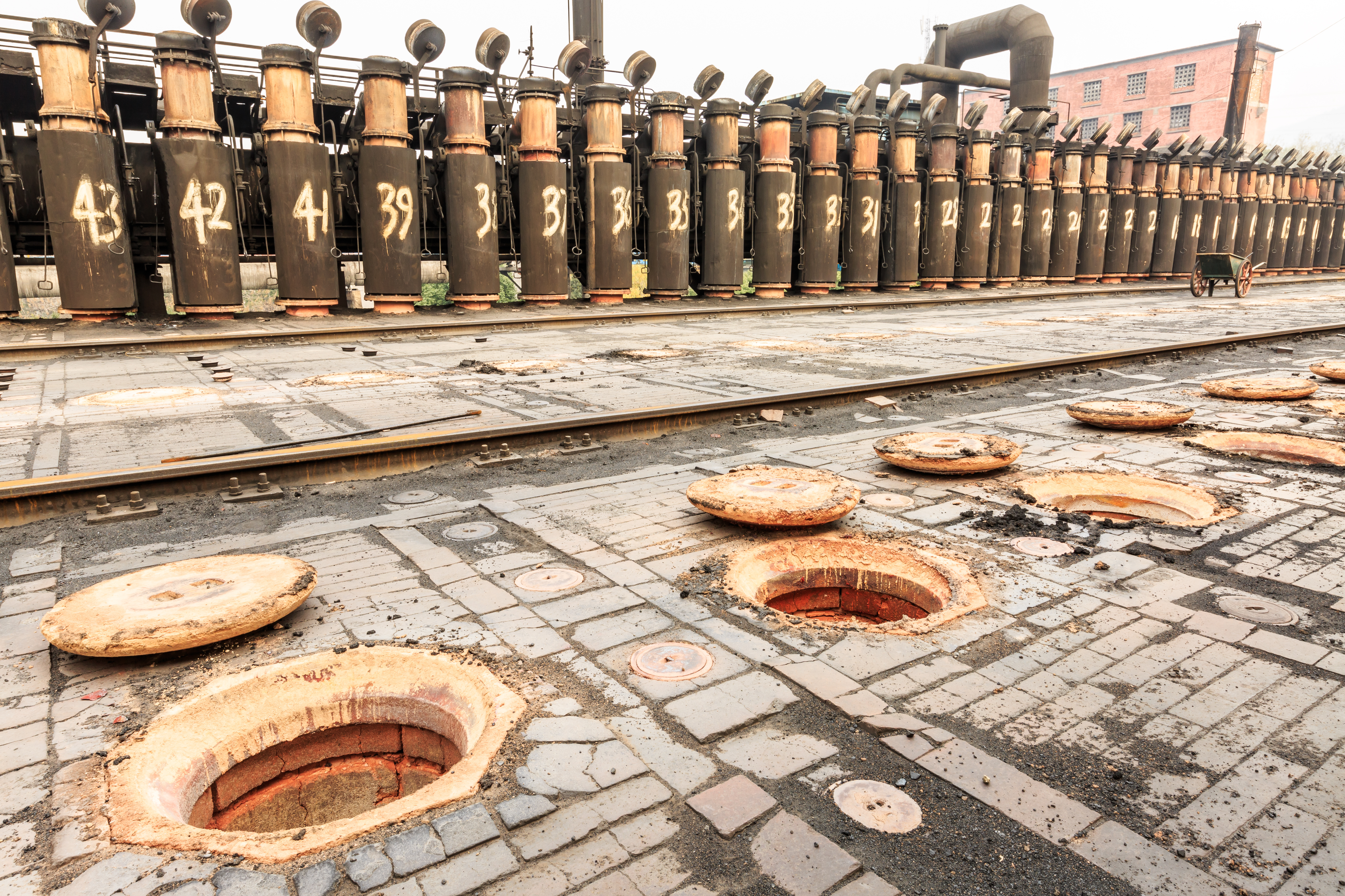 KJ Reports, China — A wide-angle shot of a massive, sterile industrial refining facility in China with workers in protective gear handling rare-earth oxides