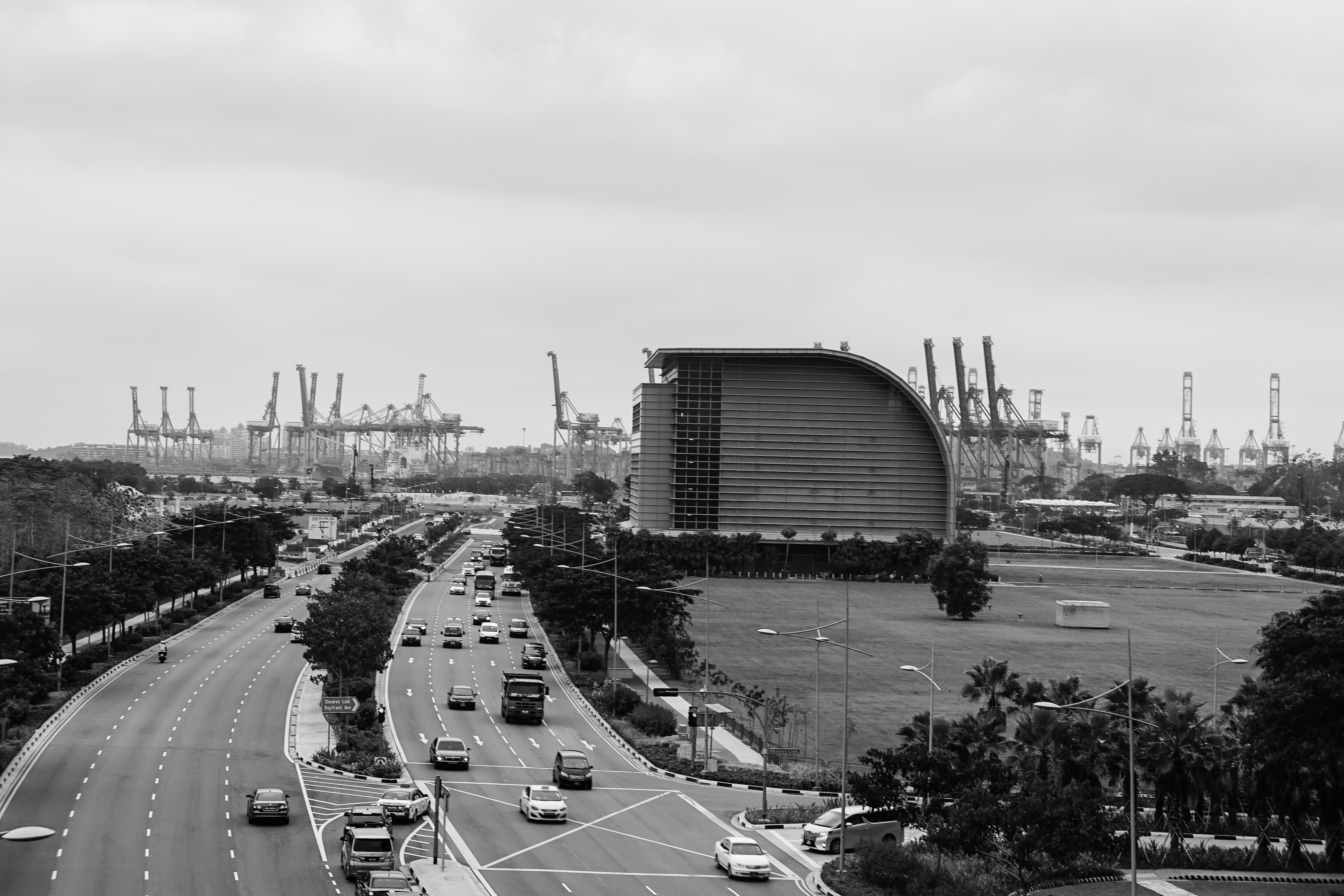 KJ Reports, Southeast Asia — A wide-angle, cinematic view of the Singapore skyline at dusk, with dozens of large cargo vessels and tankers anchored in the st…